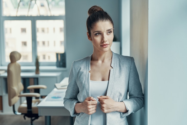 Belle jeune femme en vêtements décontractés intelligents en détournant les yeux et en ajustant la veste