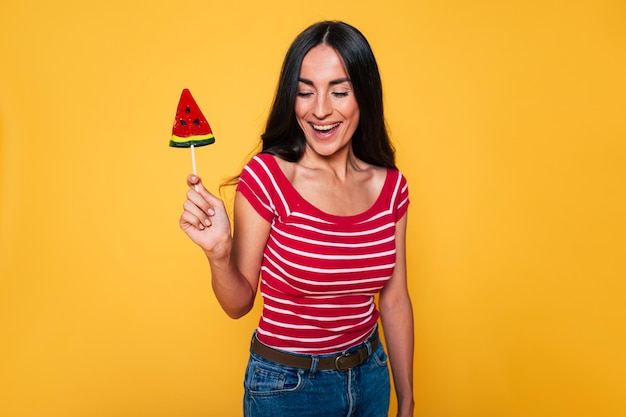 Belle jeune femme en vêtements décontractés avec sucette dans les mains posant sur fond orange