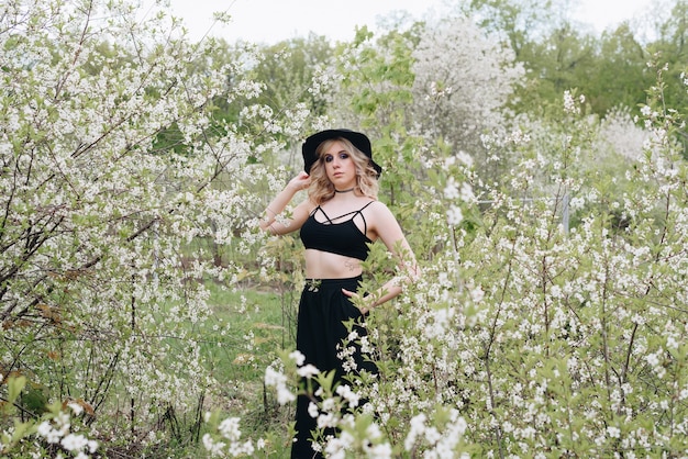 Une belle jeune femme en vêtements noirs et un chapeau dans un jardin fleuri au printemps 1