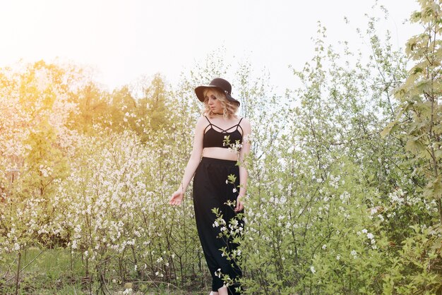 Une belle jeune femme en vêtements noirs et un chapeau dans un jardin fleuri au printemps 1