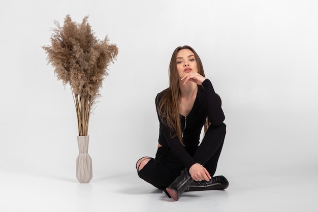 Belle jeune femme en vêtements noirs qui pose en studio sur mur gris