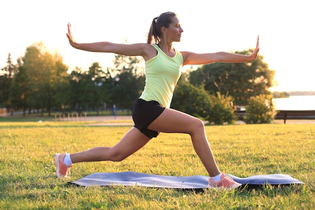 Belle jeune femme en vêtements de sport qui s'étend en se tenant debout à l'extérieur.