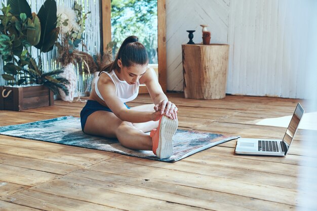 Belle jeune femme en vêtements de sport s'étendant sur le patio avec un ordinateur portable posé près d'elle