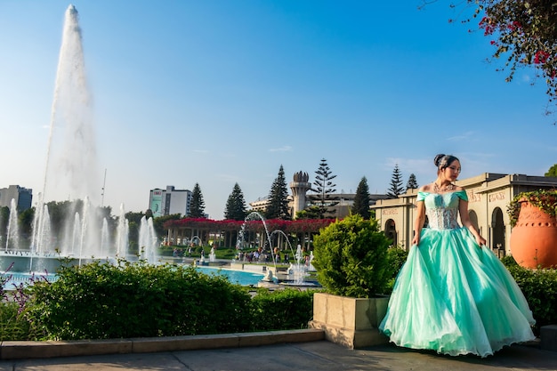 Belle jeune femme vêtue d'un costume de princesse dans un paysage de bassins d'eau et de ciel bleu.