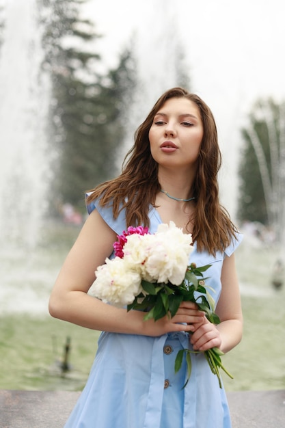 Une belle jeune femme vêtue d'une robe bleue avec un bouquet de pivoines