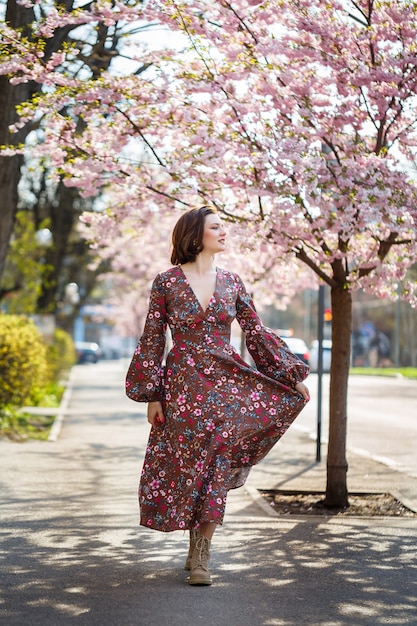 Belle jeune femme vêtue d'une robe en fleurs de sakura. C'est une chaude journée ensoleillée de printemps à l'extérieur