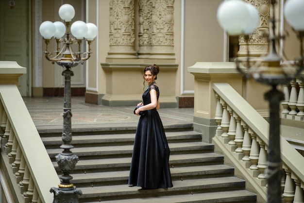 Photo belle jeune femme vêtue d'une robe noire se dresse sur les marches