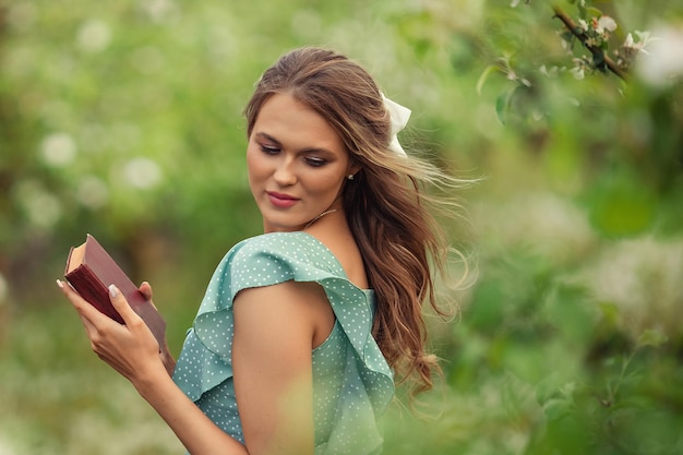 Belle jeune femme vêtue d'une robe romantique lit un deuxième livre au printemps dans un jardin fleuri