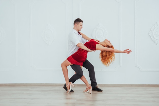 Belle jeune femme vêtue d'une robe rouge et un homme dansant isolé sur fond blanc.