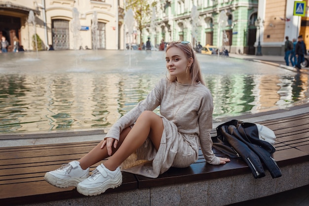 Belle jeune femme vêtue d'une robe tricotée beige se promène dans les rues de Moscou, fontaines ensoleillées du printemps dans les rues