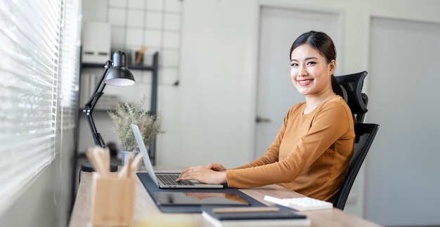 Belle jeune femme vêtue de vêtements décontractés utilisant un ordinateur portable et souriant tout en travaillant à domicile