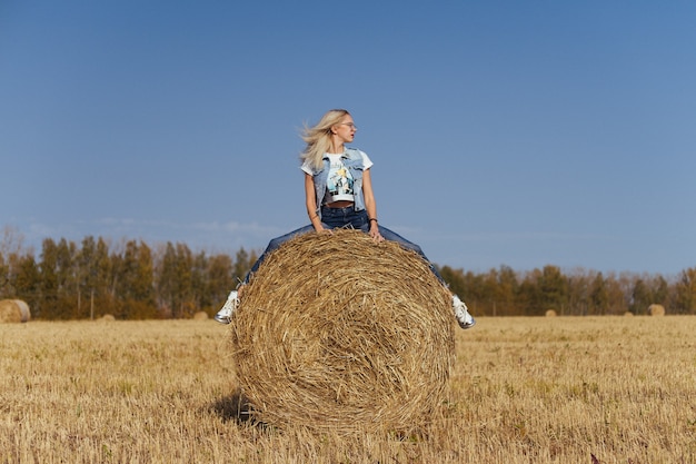 Belle jeune femme villageois posant en jeans sur une balle de foin dans un champ