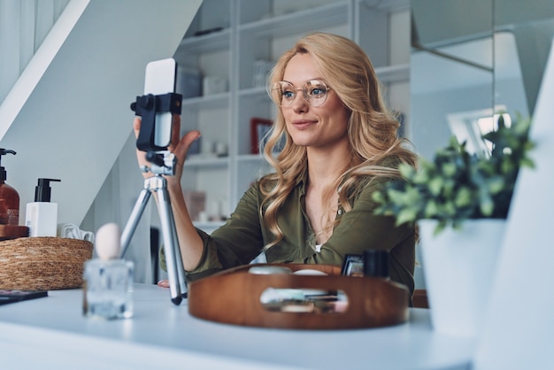 Belle jeune femme vlogging sur les produits de beauté alors qu'elle était assise au bureau à domicile