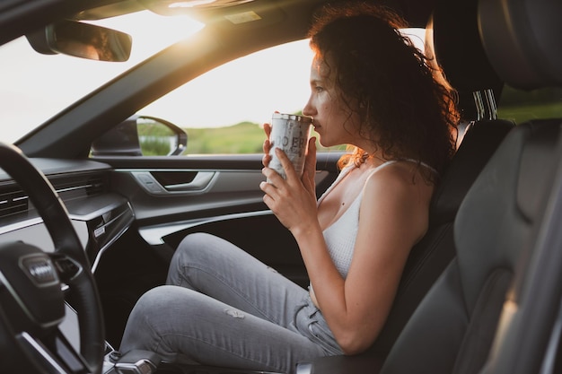 Belle jeune femme voyage sur les routes en voiture arrêtée au bord de la route et regarde la carte boire du café à partir d'un concept de vacances thermos