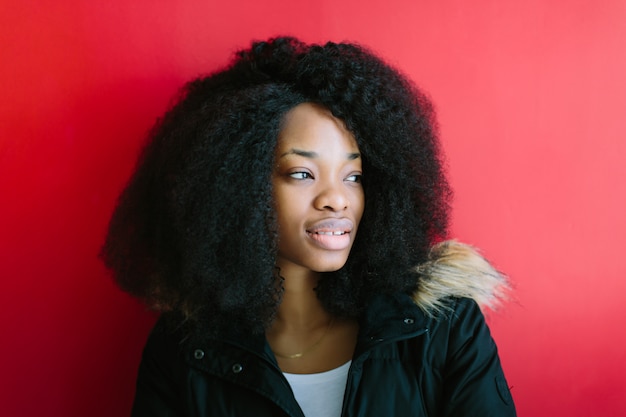 Belle jeune fille afro-américaine dans un manteau noir souriant sur fond rouge