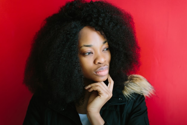 Belle jeune fille afro-américaine dans un manteau noir souriant sur fond rouge