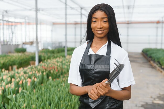 Belle jeune fille afro-américaine souriante, travailleur avec des fleurs en serre.