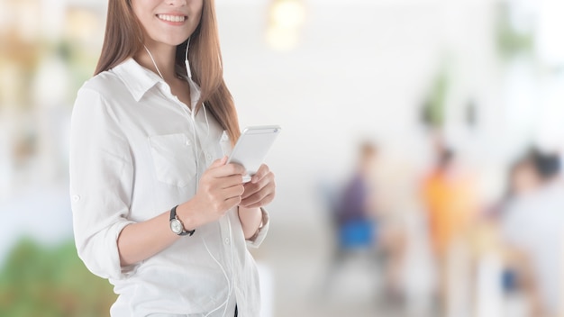 Belle jeune fille asiatique à l&#39;aide de téléphone intelligent avec écouteur en fond de restaurant