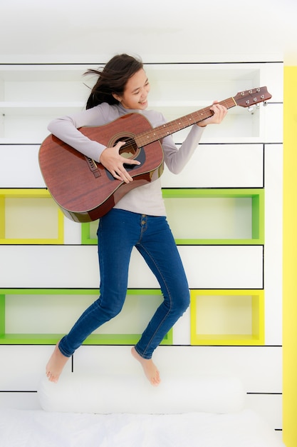 Une belle jeune fille asiatique tient de la guitare et saute dans sa chambre, utilisant son temps privé en tant qu'adolescente