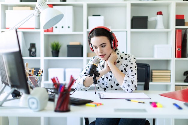 Belle jeune fille assise dans les écouteurs et avec microphone à table au bureau et parler