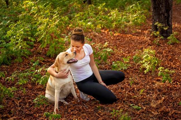 belle jeune fille assise dans la forêt avec un chien et caresser son animal de compagnie bien-aimé