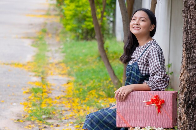 Belle jeune fille assise sous l'arbre avec coffret cadeau.