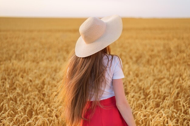 Belle jeune fille au chapeau marchant dans le champ de blé Vue arrière