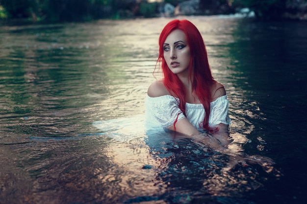 Belle jeune fille au repos dans l'eau. Jeune femme à la robe blanche est assise sur la pierre au milieu d'un ruisseau.