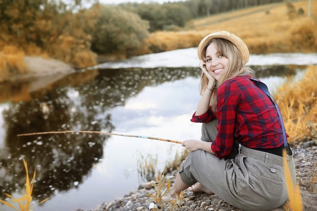 Photo belle jeune fille en automne au bord de la rivière avec une canne à pêche