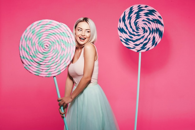 Belle jeune fille aux cheveux blonds portant haut et jupe debout avec d'énormes sucettes sucrées à rose