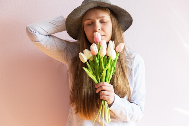 Une belle jeune fille aux cheveux longs blonds dissous un chapeau de feutre sur la tête garde les fleurs de printemps