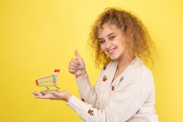 Une belle jeune fille aux cheveux roux bouclés tient un chariot de nourriture dans ses mains Concept de magasinage