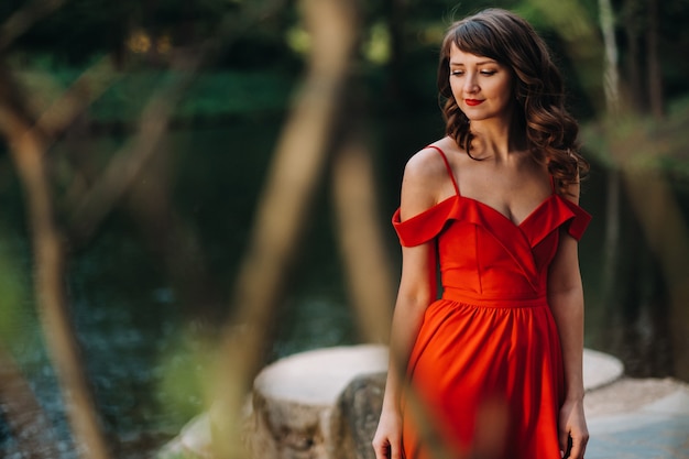 Une belle jeune fille aux longs cheveux bruns, dans une longue robe rouge avec un anneau autour du lac.