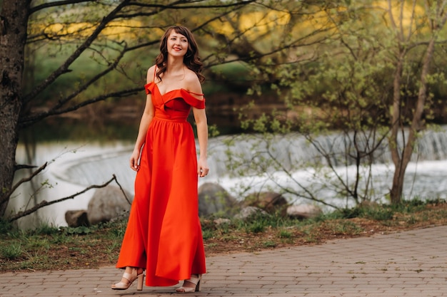 Une belle jeune fille aux longs cheveux bruns, dans une longue robe rouge avec un anneau autour du lac.