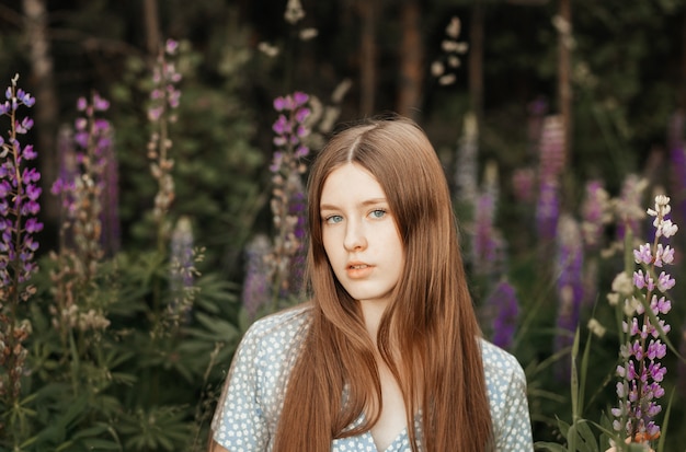 Une belle jeune fille aux longs cheveux roux dans une clairière parmi les fleurs. Lupins