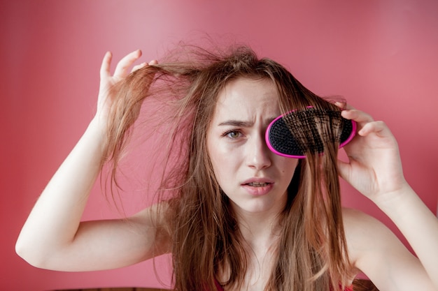 Belle jeune fille ayant des problèmes tout en cheveux sur fond rose