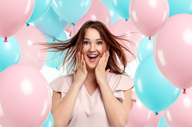 Belle jeune fille avec des ballons bleus et roses sur un mur rose.