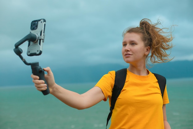 Belle jeune fille blogueuse à l'extérieur marchant en voyageant en randonnée tenant un stabilisateur ou un cardan avec