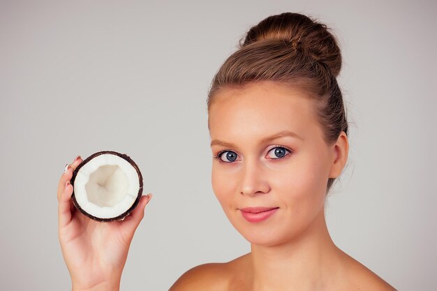 Belle jeune fille blonde de coiffure avec noix de coco dans sa main épaules nues nues en studio sur fond blanc. Beauté des cheveux et de la peau.