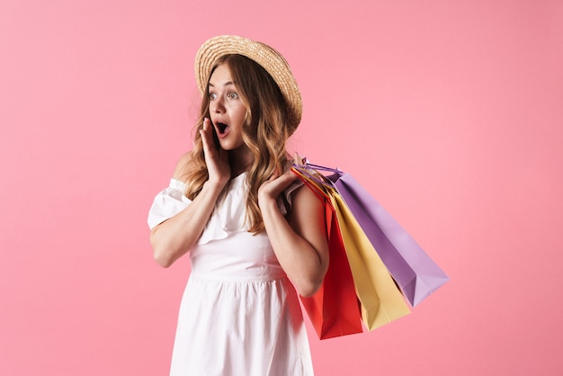 Belle jeune fille blonde joyeuse vêtue d'une robe d'été isolée sur un mur rose, portant des sacs à provisions