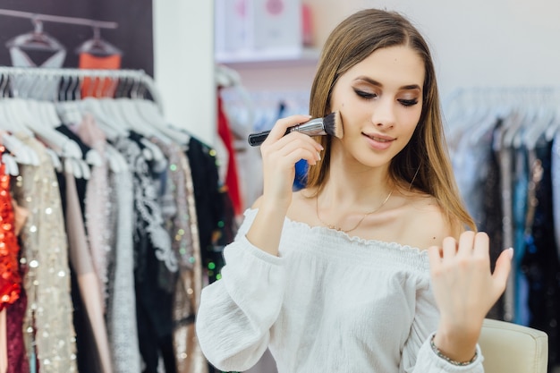 Une belle jeune fille blonde se maquille devant le miroir