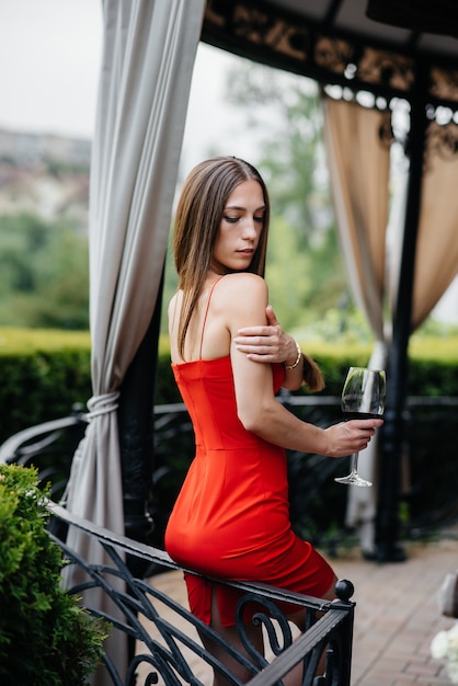 Belle jeune fille boit du vin sur la véranda d'une belle maison. Vacances.