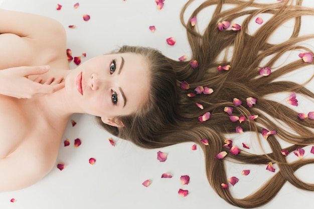 Photo belle jeune fille en bonne santé couchée sur un fond blanc avec des cheveux longs et des pétales de fleurs