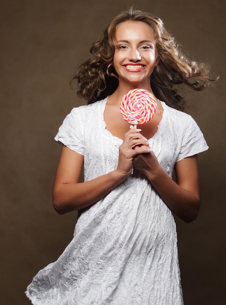 Belle jeune fille bouclée tenant une sucette blanche rouge et souriant