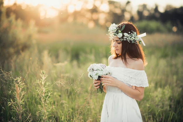 Belle jeune fille avec un bouquet de fleurs et une couronne dans une robe blanche