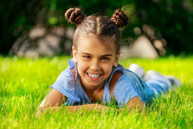 Belle jeune fille brune se trouve sur l'herbe dans le parc et sourit