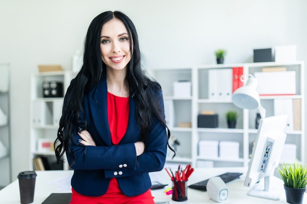 Belle jeune fille en costume est debout dans le bureau, s&#39;appuyant sur une table