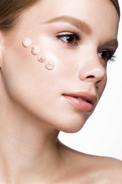 Belle jeune fille avec de la crème ton sur la peau. Beau visage. Photo prise en studio sur fond blanc.