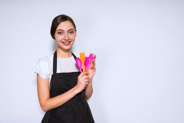 Belle jeune fille cuisinier en tablier noir aime cuisiner des aliments détient des outils pour la cuisson