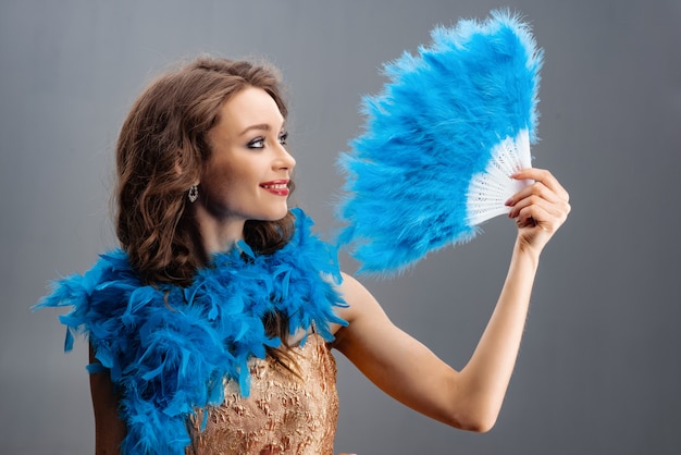 Photo belle jeune fille dans un boa bleu tenant un éventail de plumes à la main